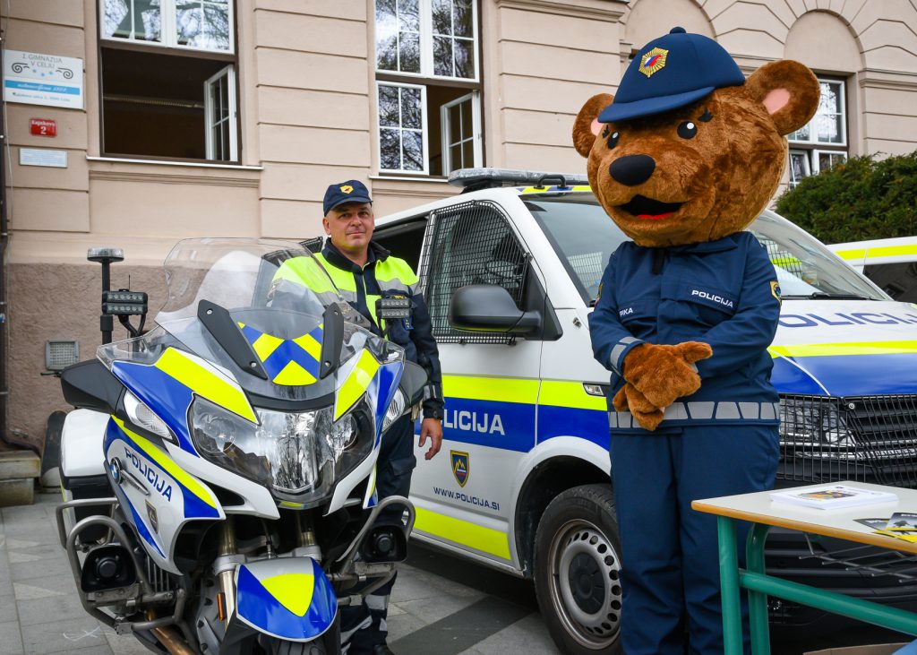 Policist z maskoto ob policijskim motorjem ter kombijem